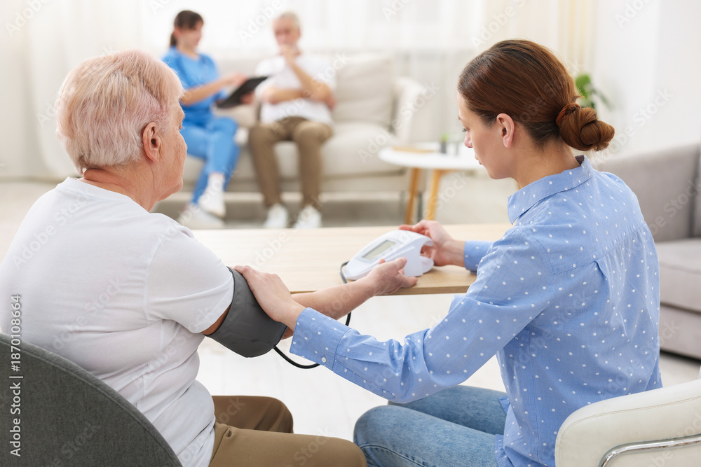 Obraz premium Caregiver measuring senior woman's blood pressure at home