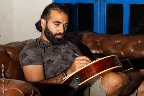 Obraz na płótnie Person writing on acoustic guitar with pen while seated on leather couch
