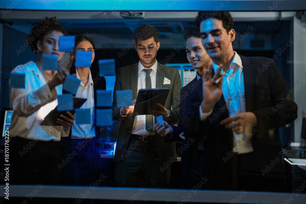 Obraz premium Corporate marketing team planning business growth strategy. Executives analyzing financial goals and market trends using sticky notes on glass wall in modern office.