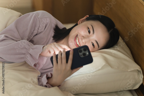 Obraz na płótnie 布団の中でスマートフォンを操作する若い女性　ライフスタイルイメージ