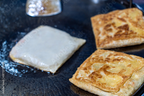 Close-up process of frying Roti Mataba (stuffed flatbread) and crispy roti on a large flat iron pan at a street food stall in Thailand.