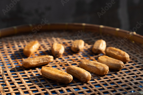 High-angle view of sun-dried bananas arranged on a woven bamboo tray, featuring a striking color contrast with the vivid blue background visible through the weave.