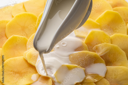 The process of making potato gratin. Delicate cream is poured over raw, thin potato slices. High quality photo