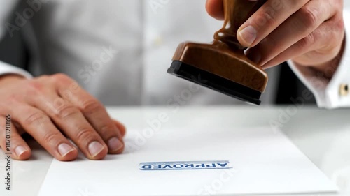 A hand stamps 'APPROVED' on a white paper. Detail on hand, stamp & cufflink visible
