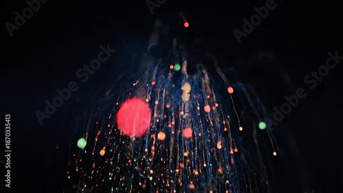 A burst of colorful particles erupts against a black background, with streaks and dots