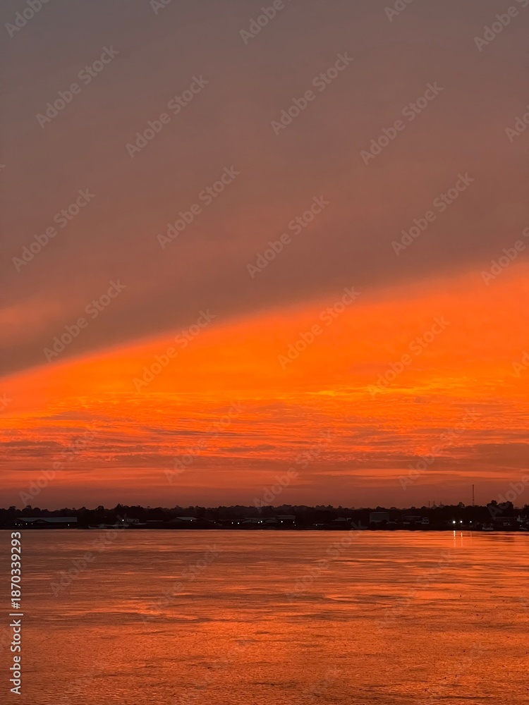 Fototapeta premium A wide-angle landscape shot of a dramatic sunset over a wide river.