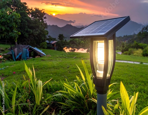Illuminated solar lamp in a lush field with tents and distant mountains at sunset