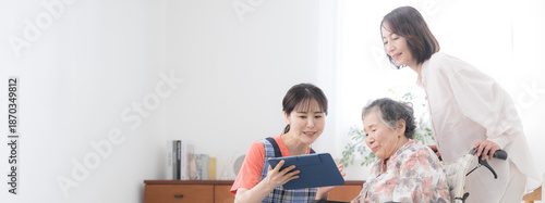 Konstfotografi 在宅介護や訪問介護のデイサービスのイメージで訪問する看護師と後期高齢者の女性と家族　訪問介護の計画などをタブレットで案内するバナー