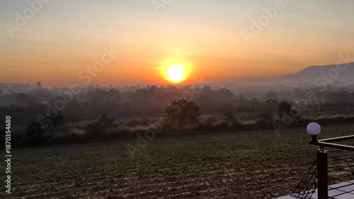 4K VIDEO footage. Experience breathtaking sunrise over misty countryside. Time-lapse captures sun rising over rolling hills and fog-covered fields filling sky with vibrant orange hues