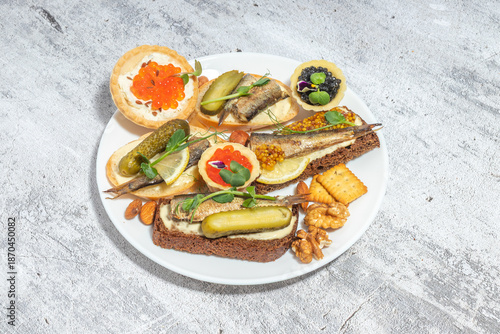 An appetizing plate of assorted canapés with fish, pickles, nuts, and crackers presented on a textured background.