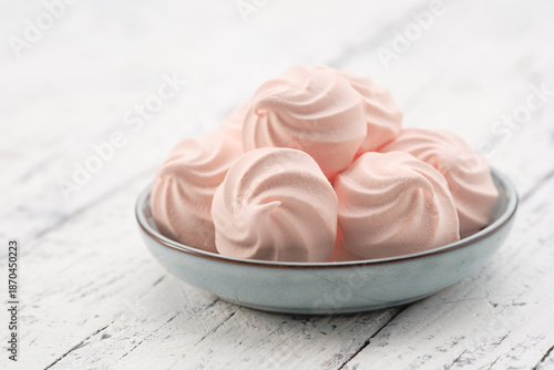 Close up of several pink homemade zefir marshmallow confection in a small blue bowl, served on a distressed white rustic wooden table. Meringue cookies  on a plate. Copy space for text.