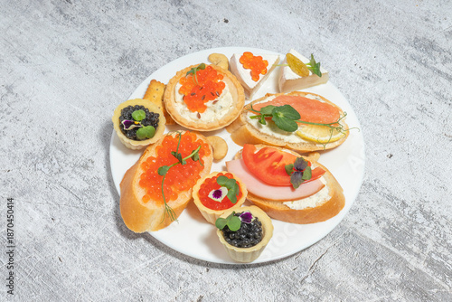 An elegant assortment of canapés on a white plate featuring various toppings like caviar, salmon, and cheese over a textured background.