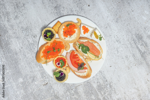 Plate with various appetizers including caviar, salmon, and vegetables on rustic background