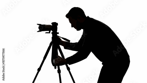 Silhouette of a photographer adjusting a camera on a tripod.