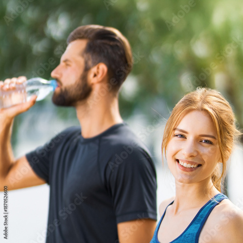 Portrait image - happy smile couple cute woman, man hold plastic water drink bottle coach trainer, after successful summer morning run training at park nature. Fitness, sport, workout concept. Square