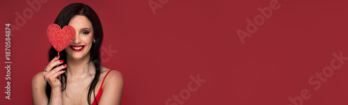 Banner with beauty studio portrait of young beautiful woman holding red heart against red background
