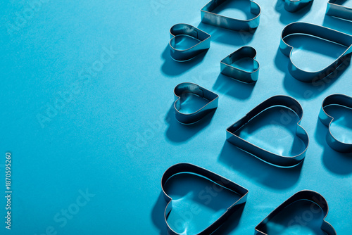 High angle view of heart shape pastry cutters with shadows by copy space on blue background