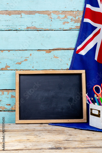 Blank writing slate by australian flag and desk organizer against old wooden wall with copy space