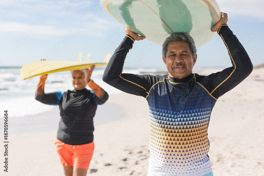 Fototapeta premium Multiracial senior couple carries surfboards at beach, enjoying retirement