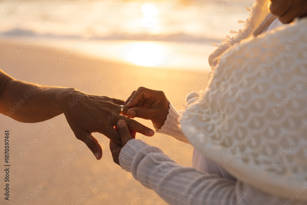 Fototapeta premium Midsection of senior bride putting ring on bridegroom's finger at beach wedding ceremony