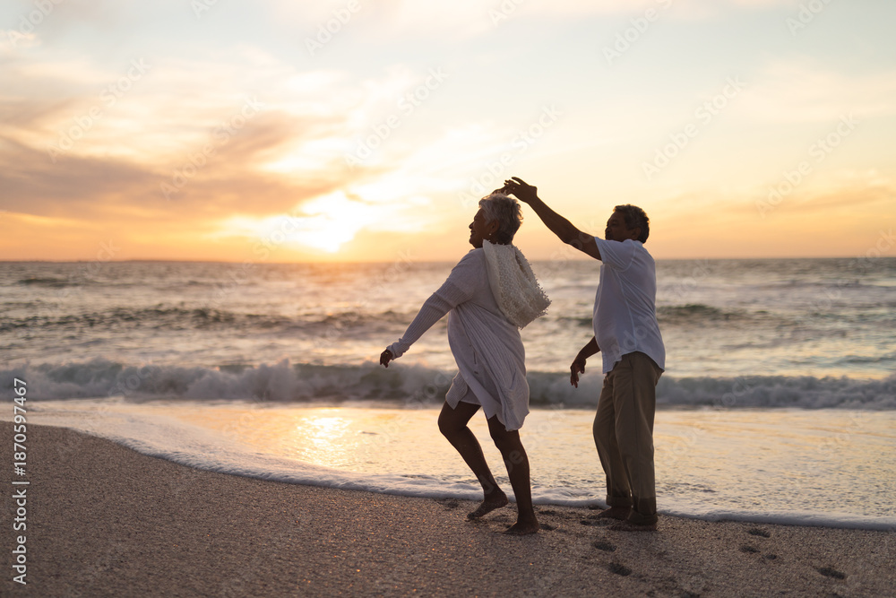 Obraz premium Full length of happy senior multiracial couple dancing on shore at beach against sky during sunset