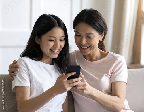 Mother and daughter share a phone, smiling together indoors