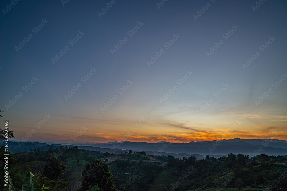 Obraz premium A breathtaking view of a colorful sunset over layered mountain silhouettes, with warm hues of orange, pink, and blue blending seamlessly across the sky.