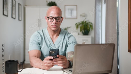 Smiling Healthcare Professional in Scrubs Engaged with Smartphone at Home Office Desk