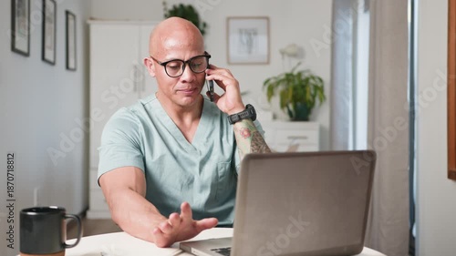 Bald Doctor Consults Remotely on Phone While Using Laptop in a Bright Home Office
