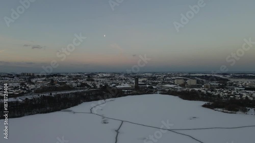 Aerial drone footage showing suburban residential areas during sunrise in winter. The scene features houses, streets, and surrounding neighborhoods under winter conditions, with early morning light il