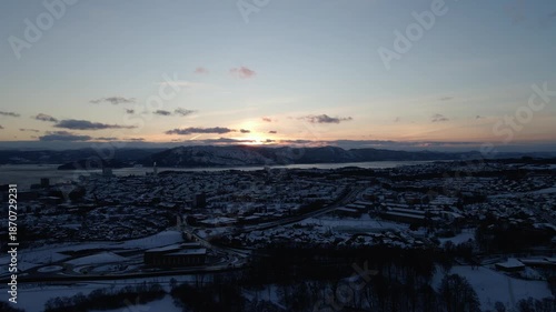Aerial drone footage showing suburban residential areas during sunrise in winter. The scene features houses, streets, and surrounding neighborhoods under winter conditions, with early morning light il