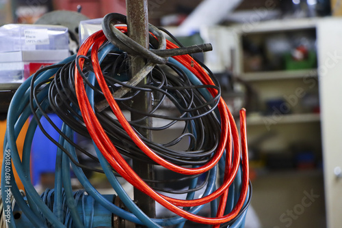Obraz na płótnie Messy electrical wires hanging on metal rod in industrial workshop with colorful