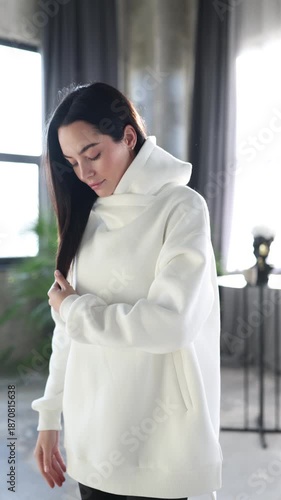 Young woman in white oversized hoodie posing in studio and putting hands in pockets