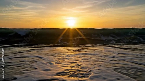 Golden sunset over the ocean with waves crashing on the shore, creating a serene seascape.
