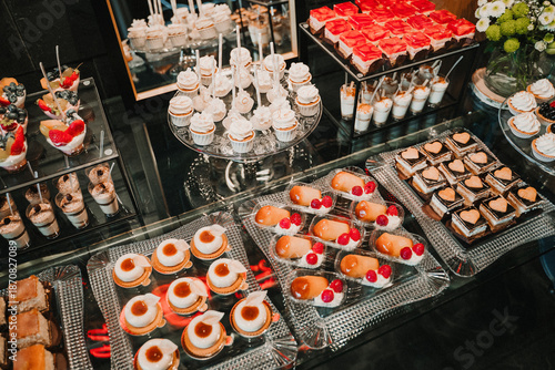 Elegant dessert table with layered mini desserts in glass cups prepared for wedding reception or luxury event. Sweet buffet with chocolate and berry desserts arranged in rows on catering table, perfec