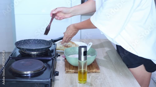 A person prepares to cook another pancake by greasing a hot skillet, pouring in batter, and swirling it evenly across the pans surface.