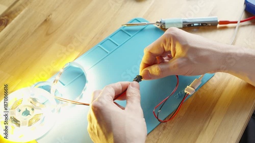 Close-up of male hands connecting wire plugs on a silicone soldering mat, powering on an LED strip on the workbench, electronics assembly and lighting test