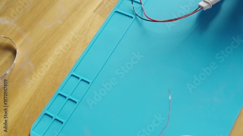 Top view close-up of solder wire touched by a hot soldering iron tip, white smoke rising during electronics work on a blue silicone soldering mat.