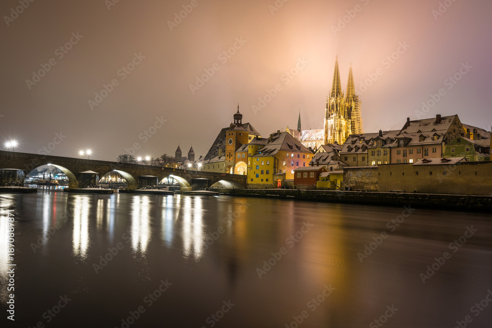 Obraz premium Regensburg mit Domblick auf Dom Sankt Peter und Steinerne Brücke nachts im Winter mit Schnee und Beleuchtung, Deutschland