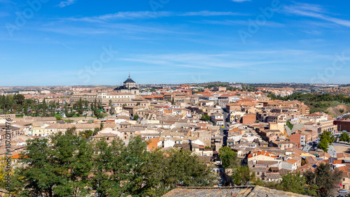 Panoramic cityscape of Toledo with traditional Spanish residential architecture and the Colegio de San Juan Bautista under a blue sky, Spain