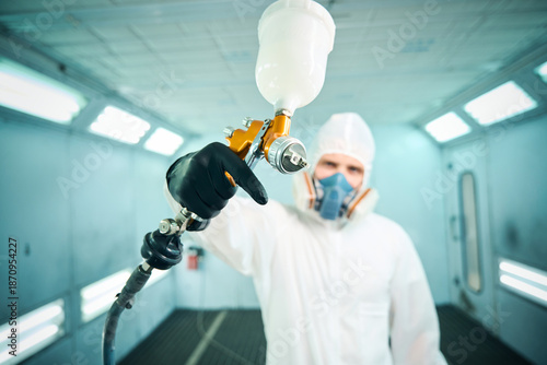 Male car mechanic working with spray gun painting on auto body