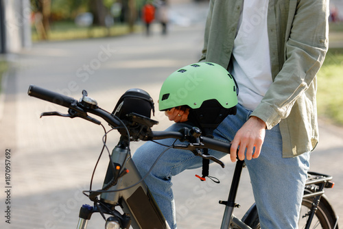 Man wearing green helmet prepares for bike ride at park during sunny day in afternoon