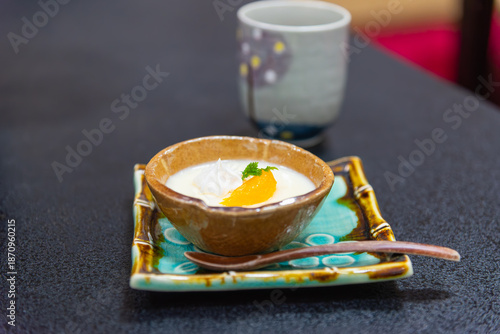 Japanese dessert pudding with orange and cream in a ceramic bowl served with tea. Authentic oriental sweet snack for cafe and restaurant menu background.