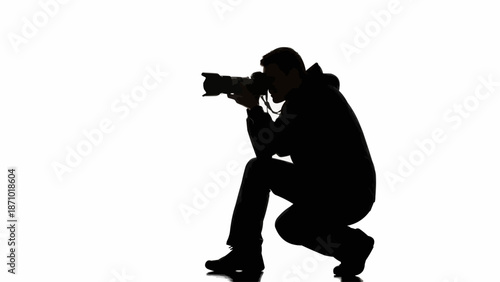 Silhouette of a photographer crouching and taking a picture with a professional camera.