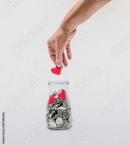 Woman hand puts red heart into transparent jar with silver coins. Compassion concept.