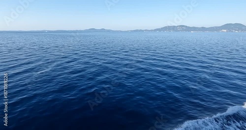 Expansive deep blue ocean with gentle ripples and distant coastal hills under clear sky.