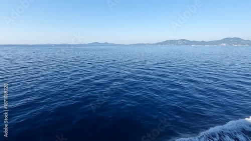 Expansive deep blue ocean with gentle ripples and distant coastal hills under clear sky.