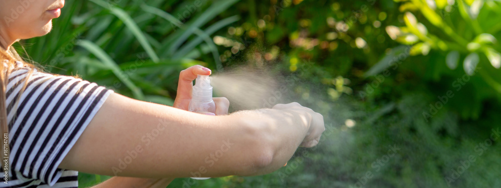 Fototapeta premium Woman applying protective spray on her arm in the garden. Insect repellent or sunscreen