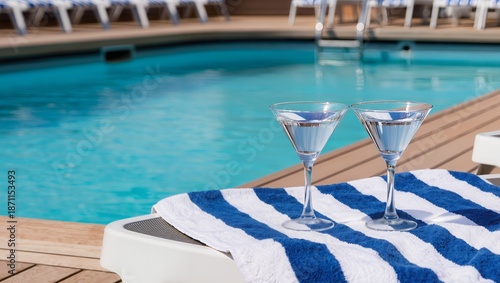 Relaxing cruise resort pool scene with martini glasses on striped towel at sunlit deck chairs, clear blue water, luxury hotel vacation concept for travel, leisure, summer escape