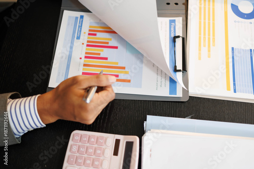 A man is holding a piece of paper with a pie chart on it. He is pointing at the chart and seems to be explaining something to someone. Concept of importance and focus
